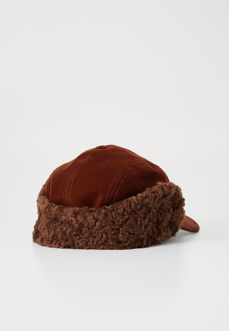 Brown cap with a corduroy top and a fluffy, textured fur band around the bottom. Features a curved brim and stitched detailing on the top.