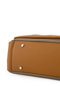 Tan leren tas met een gladde textuur, voorzien van zilveren hardware-accenten en een contrasterende beige afwerking langs de randen.