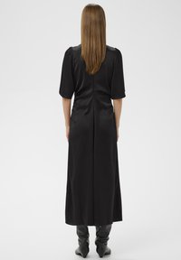 Must vest, mille kaheksa kätetuharate, sujuva tekstuuriga ja figuuri rõhutava vöökohaga. Rõhutatud puhta ja minimalistliku kujundusega. Kandmine põlvekõrguste saapadega.