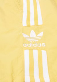 Yellow jacket featuring white horizontal stripes and a white embroidered Adidas logo. Made of lightweight material with a smooth texture.