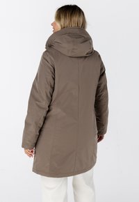 Bruine puffercoat met een hoge kraag en capuchon, met een gladde textuur en een rechte snit, tot halverwege de bovenbenen, gedragen over lichtgekleurde broek.