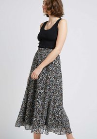 Jupe florale noire avec un design fluide en A, pr�ésentant un mélange de fleurs bleues, jaunes et crème sur un fond noir. Associée à un débardeur noir.