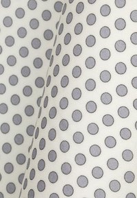 Biała tkanina z równomiernie rozmieszczonymi szarymi kropkami. Kropki są okrągłe i mają lekko teksturowaną powierzchnię, co tworzy efekt warstwowości.