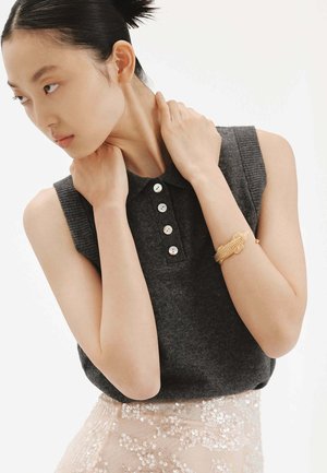 Top sin mangas de color gris oscuro con cuello tipo polo, que presenta cinco botones blancos y textura acanalada, combinado con una falda ligera rosa con lentejuelas.