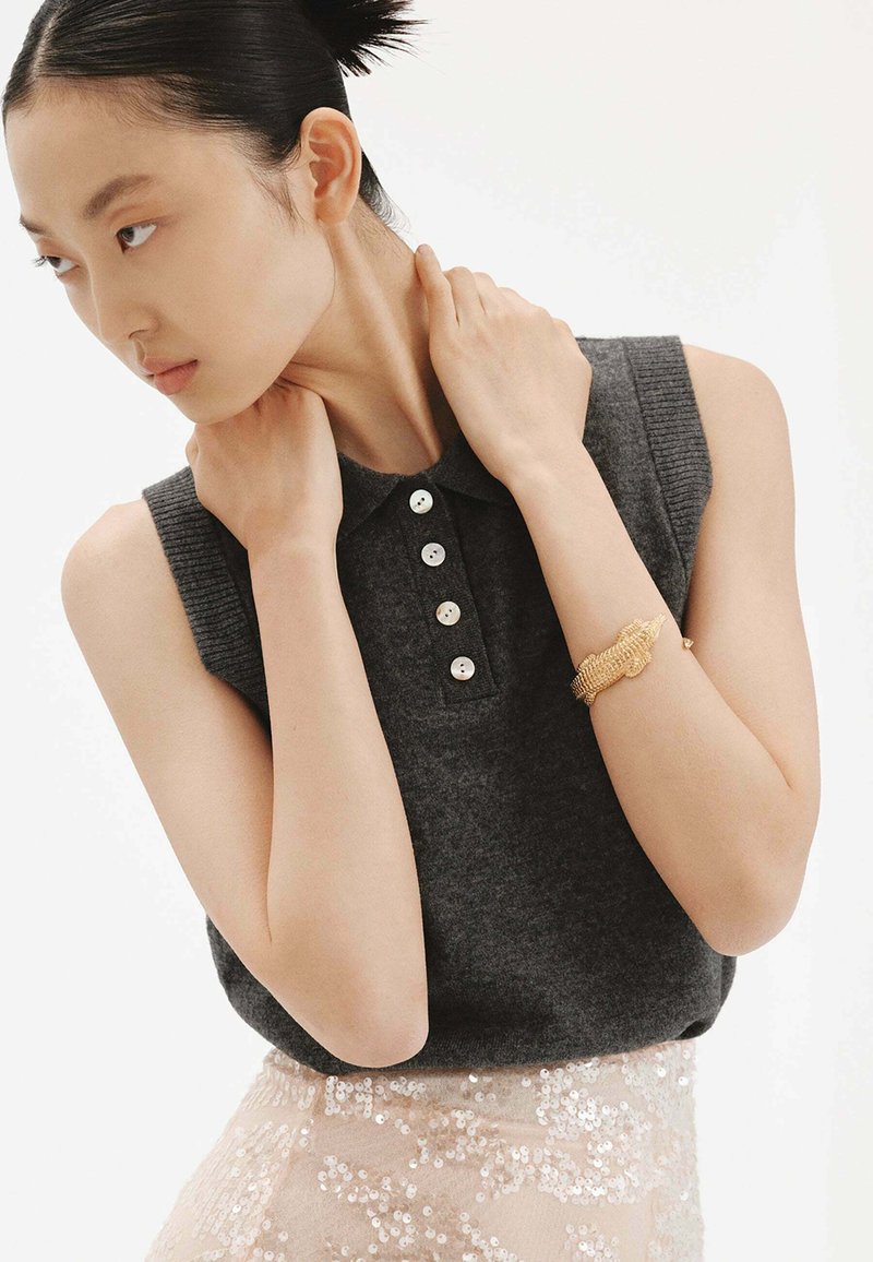 Top sin mangas de color gris oscuro con cuello tipo polo, que presenta cinco botones blancos y textura acanalada, combinado con una falda ligera rosa con lentejuelas.