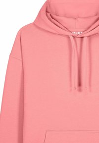 Felpa con cappuccio rosa realizzata in morbido tessuto. Presenta una tasca frontale, cordini e polsini a coste. Dettaglio di cuciture minimale.