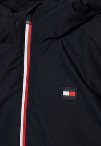 Námořnická bunda s kapucí a předním zipem, s červenými a bílými pruhy a obdélníkovou nášivkou v červené, bílé a modré barvě.