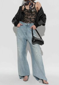 Donna con top in pizzo nero, giacca di pelle nera, jeans larghi a vita alta con strappi chiari, borsa nera, sandali con tacco alto argentati e foulard con fantasia al collo.