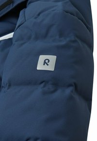 Marineblaue Steppjacke aus Material mit glatter Textur; verfügt über ein silbernes Logo am Ärmel und einen kontrastierenden weißen Reißverschluss.