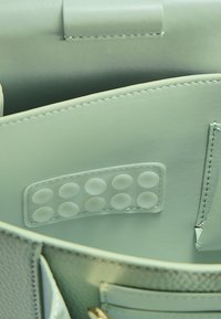 Interno di una borsa a mano in pelle verde chiaro con una superficie liscia, pannello per impugnatura circolare in silicone e numerosi scomparti.
