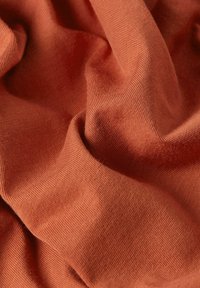 Tessuto testurizzato in un caldo colore terracotta, caratterizzato da una superficie morbida a maglia con sottili variazioni di tonalità e pieghe delicate.