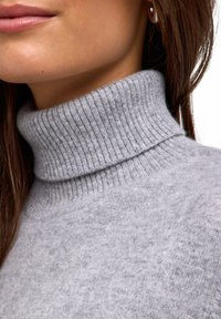 Maglione grigio a collo alto realizzato in morbido materiale a maglia, con un colletto a coste spesso e una superficie liscia, caratterizzato da un delicato motivo a macchie.