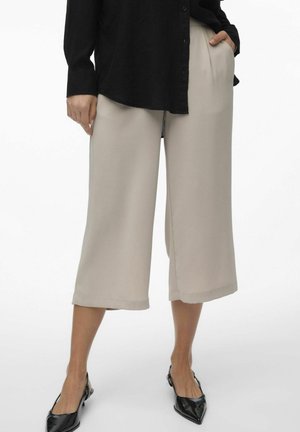 Pantaloni beige a gamba larga con una texture liscia, dotati di tasche laterali e una vestibilità rilassata. Abbinati a ballerine nere a punta.