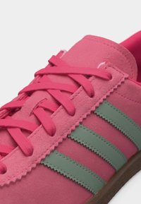 Κοντινό πλάνο ροζ σκαρπίνι από σουέντ με πράσινες λωρίδες, ροζ κορδόνια και καφέ σόλα, που δείχνει λεπτομερή ραφή και υφή.