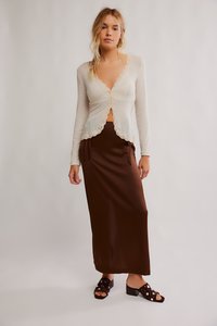 Gaiši bēša, garām piedurknēm topiņš ar viļņotu mežģīņu apmali, kombinēts ar brūnu satīna svārku ar auklām. Melnas slaidu sandales ar rotājumiem.