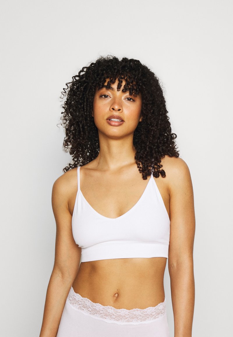 Bralette bianco in cotone con spalline sottili regolabili e scollatura a V. Abbinato a slip a vita alta in pizzo rosa chiaro.