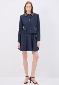 Šitá dvoudílná souprava v tmavě modré pruhované látce. Zkrácená bunda s hnědým límcem a akcenty kapes, spárovaná s rozšířenou sukní.
