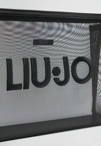 Črna mrežasta kozmetična torbica z enobarvnimi črnimi vezenimi črkami "LIU•JO", ki je vidno na sprednji strani, z teksturiranimi akcenti.