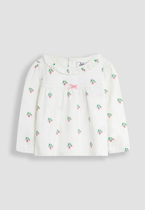 Maglietta bianca a maniche lunghe con colletto a volant, caratterizzata da un fiocco rosa e motivi di fragole verdi e rosa sparsi. Tessuto morbido e leggero.