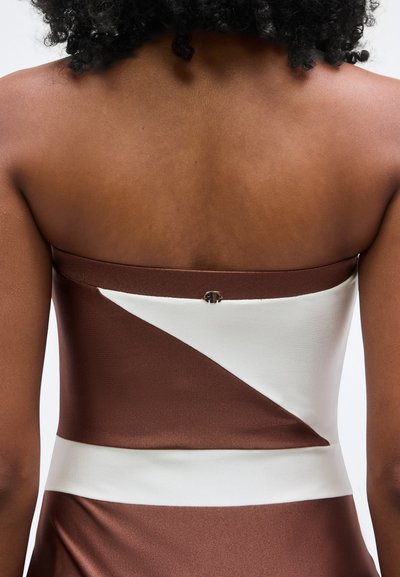 Barna és fehér pánt nélküli ruha testhezálló felsőrésszel. A sima, fényes anyag átlós fehér betéttel és hátul kapcsos záródással rendelkezik.