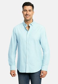 Camisa de botones azul claro con tejido texturizado, mangas largas y cuello clásico. Presenta un dobladillo curvo y botones en contraste.
