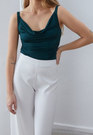 Teal mouwloze top met een gedrapeerde halslijn, gecombineerd met witte, hooggetailleerde broek. Gladde stof, minimalistisch ontwerp en strakke pasvorm.