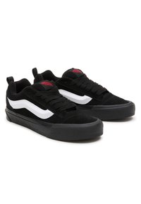 Sneaker in suede nero con design a swoosh bianco, suola piatta in gomma nera e logo rosso sul linguetta; allacciate con lacci rotondi neri.