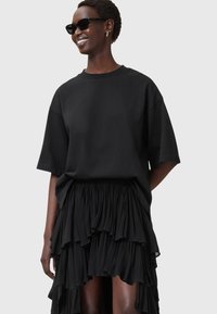 Sort oversized t-shirt parret med en lagdelt sort nederdel. Begge beklædningsgenstande har en glat tekstur og en afslappet pasform, hvilket fremhæver kontrasten i designet.