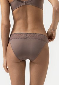 Woman's back and lower torso wearing mauve lace-trimmed underwear and a matching bra, standing against a plain white background.