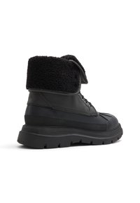 Black waterproof boots with a textured black fleece cuff, sturdy rubber sole, and lace-up front, featuring a smooth and matte finish.
