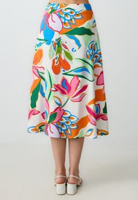Een knie-lange rok van witte stof met een levendige bloemenprint in roze, oranje, groen en blauwe details, gecombineerd met witte blokhakken.