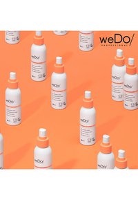 Bottiglie spray bianche con tappi e etichette arancioni, con informazioni sul prodotto, disposte su uno sfondo arancione.