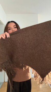 Sciarpa spessa marrone realizzata in tessuto testurizzato, con bordi sfrangiati. Il tessuto ha un aspetto morbido ed è sollevato per mostrare la sua forma e dimensione.