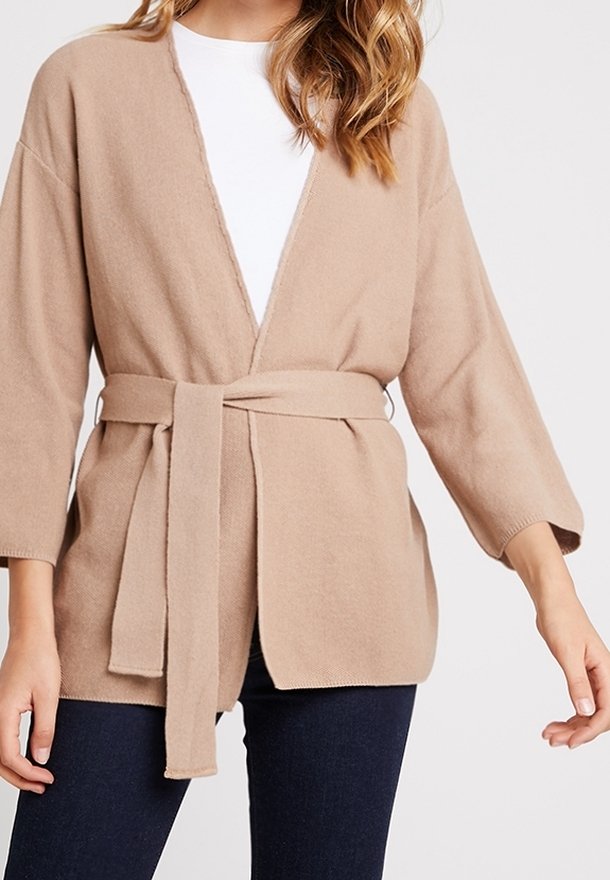 Cardigan beige ceinturé porté sur un haut blanc avec un pantalon bleu foncé, présenté sur une personne des épaules aux hanches.