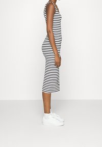 Robe midi rayée noir et blanc avec fines bretelles, coupe ajustée et fentes latérales. Portée avec des baskets blanches pour un look décontracté.