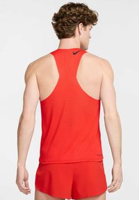 Punane sportlik tank top, millel on võidusõidukaela disain. Valmistatud hingavast materjalist, mis sisaldab võrkkangast ja väikeseid avausi ventilatsiooniks.