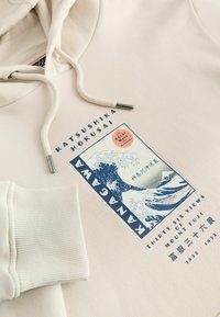 Beige hoodie med et trykt design af Hokusais "Den Store Bølge ved Kanagawa" samt tekst om Mount Fuji og kunstneren.