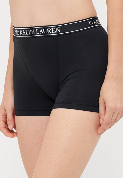 Svarte tettsittende boxer-shortser med en hvit Polo Ralph Lauren-logo i midjen, båret av en person fra midjen til midten av låret.