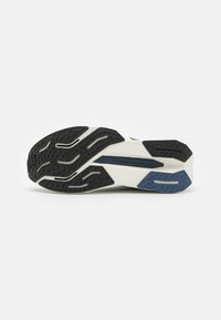 Semelle de chaussure de sport noir et blanc avec des motifs de grip texturés et un design épuré. Comprend des accents bleus et un matériau lisse et durable.