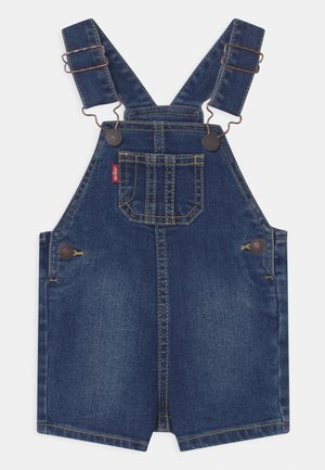 Salopette courte en jean bleu avec bretelles réglables, poche poitrine avant, boutons latéraux et surpiqûres jaunes contrastées.
