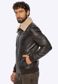 Bruine leren jas met een lichtbruine bontkraag, ritssluiting, geribbelde manchetten en twee voorzakken. Soepele textuur en een getailleerd ontwerp.