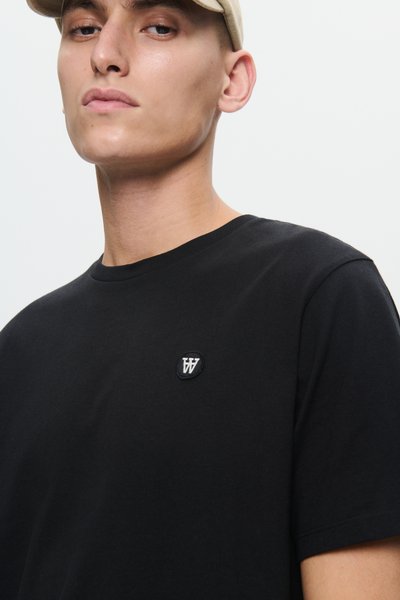 Camiseta de algodón negra con cuello redondo y un pequeño parche de logo bordado en el lado izquierdo del pecho, textura suave, corte ajustado.