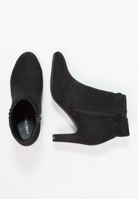 Botines de ante negros con punta afilada, tacón stiletto de altura media y detalle de cremallera lateral. Textura suave con un acabado suave.