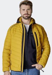 Yellow puffer jacket with horizontal quilted pattern, hood, front zip, and side pockets. Worn over a navy zip-up hoodie.