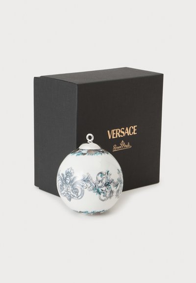 Ornement décoratif rond blanc avec des motifs bleus et gris complexes à côté d'une boîte noire de marque Versace.