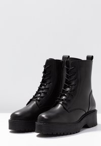 Bottes noires en cuir montant à la cheville, avec un bout arrondi, une semelle plateforme haute, des lacets sur le devant et une fermeture éclair latérale. Semelle extérieure en caoutchouc texturée avec rainures.