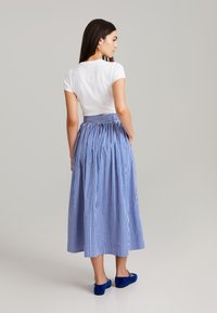 Blau-weißer Karomidirock mit gerafftem Bund, kombiniert mit einem taillierten weißen T-Shirt und blauen Ballerinas. Glatte Stofftextur.