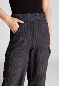 Dunkelgraue gerippte weite Hosen mit einem elastischen Bund, ausgestattet mit Seitentaschen und einer Gesäßtasche im Cargo-Stil am Oberschenkel.