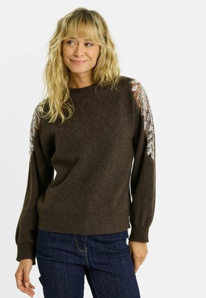 Pull marron à manches longues et col rond. Détails décoratifs avec des perles sur les épaules. Texture douce, ajusté à la taille.