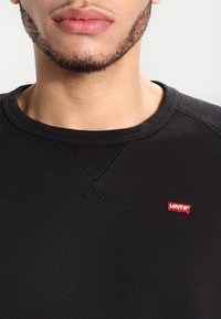 Sort langærmet crewneck-trøje med ribbet tekstur. Har et lille rødt Levi's-logo på venstre brystområde. Minimalistisk design.